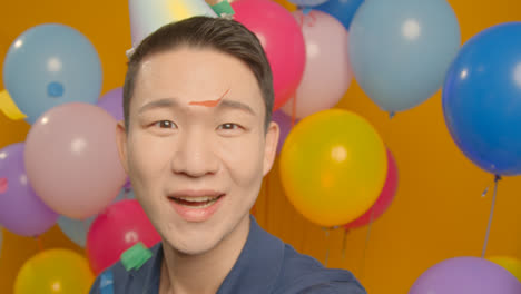 POV-Studioporträt-Eines-Mannes,-Der-Ein-Selfie-Mit-Partyhut-Macht-Und-Seinen-Geburtstag-Feiert,-Umgeben-Von-Luftballons